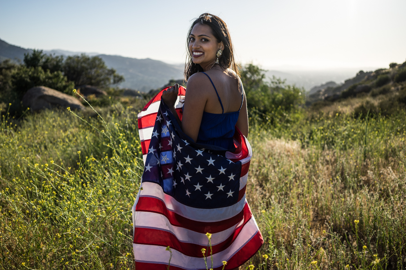American woman and flag portrait in grassy meadow landscape at sunset