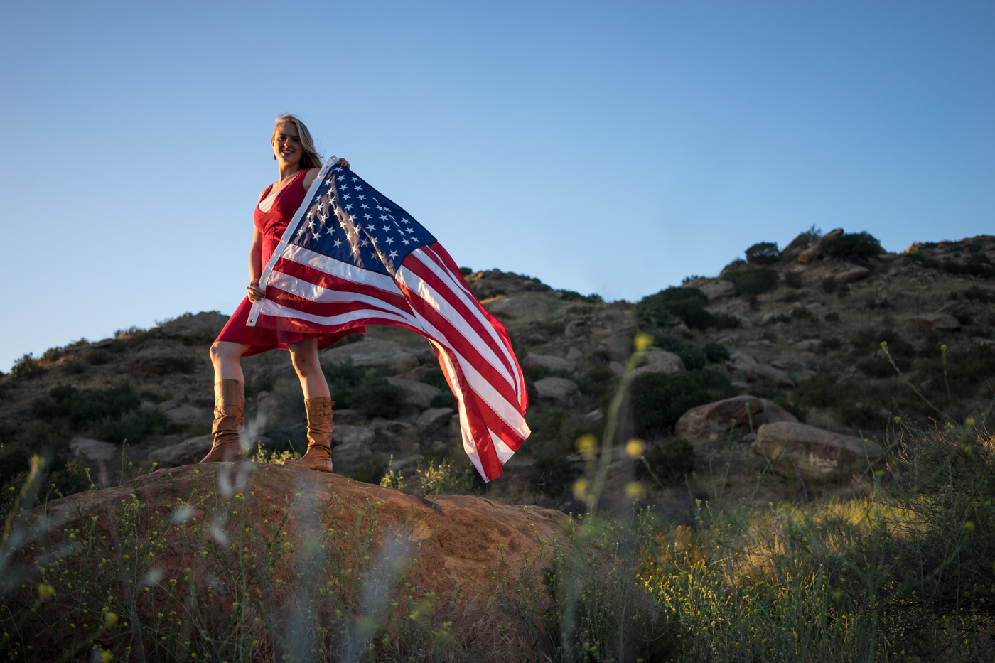 American woman with waving flag portrait in grassy mountain landscape at sunset