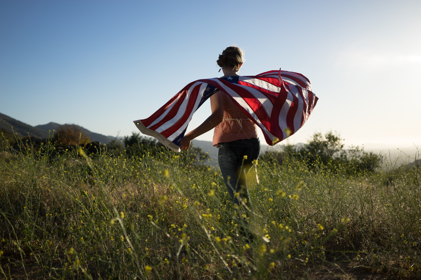 American woman with waving flag portrait in grassy mountain landscape at sunset