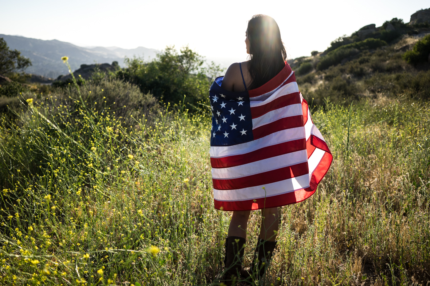 American woman with flag portrait in grassy mountain landscape at sunset